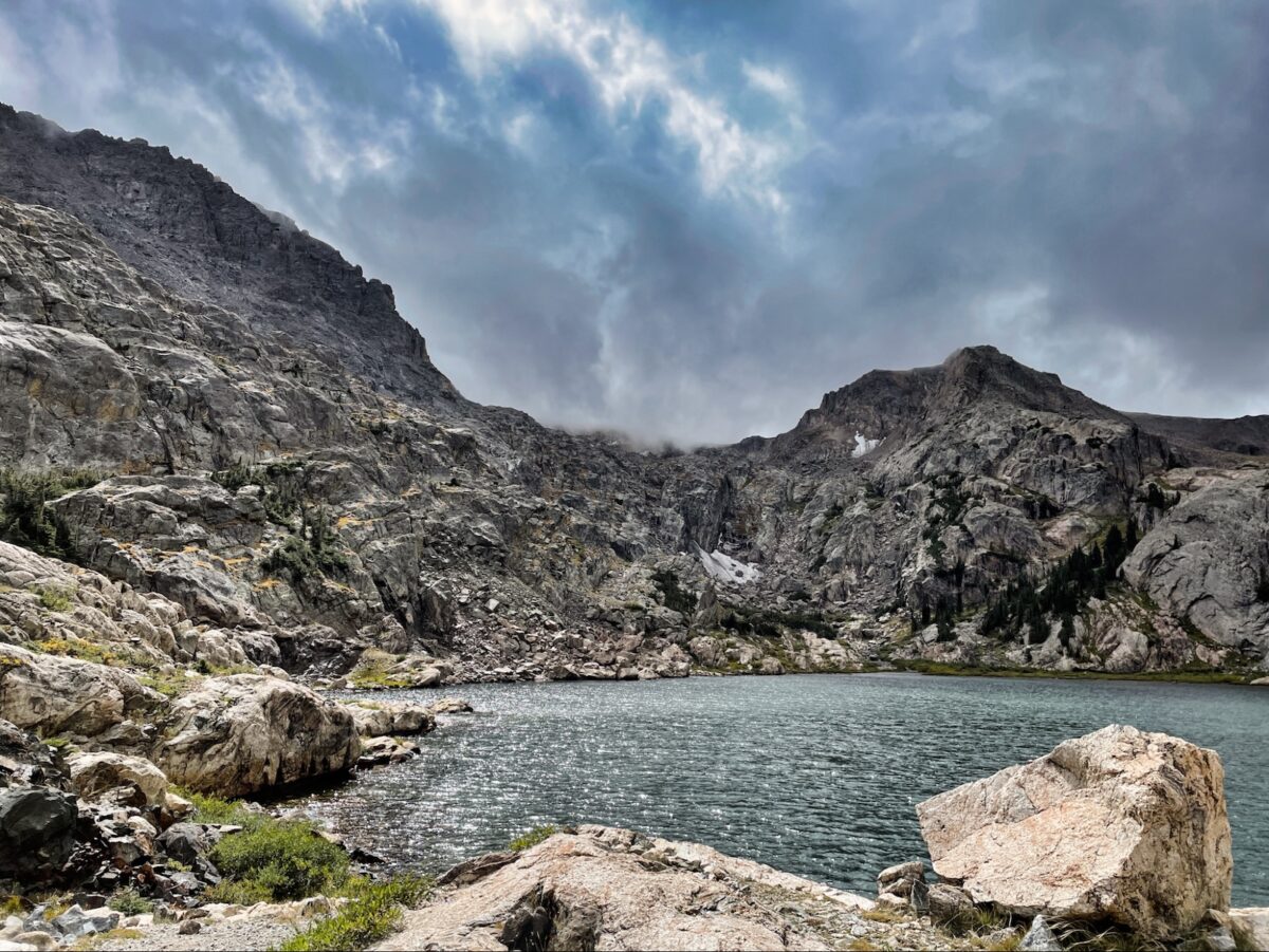 a lake surrounded by mountains under a cloudy sky