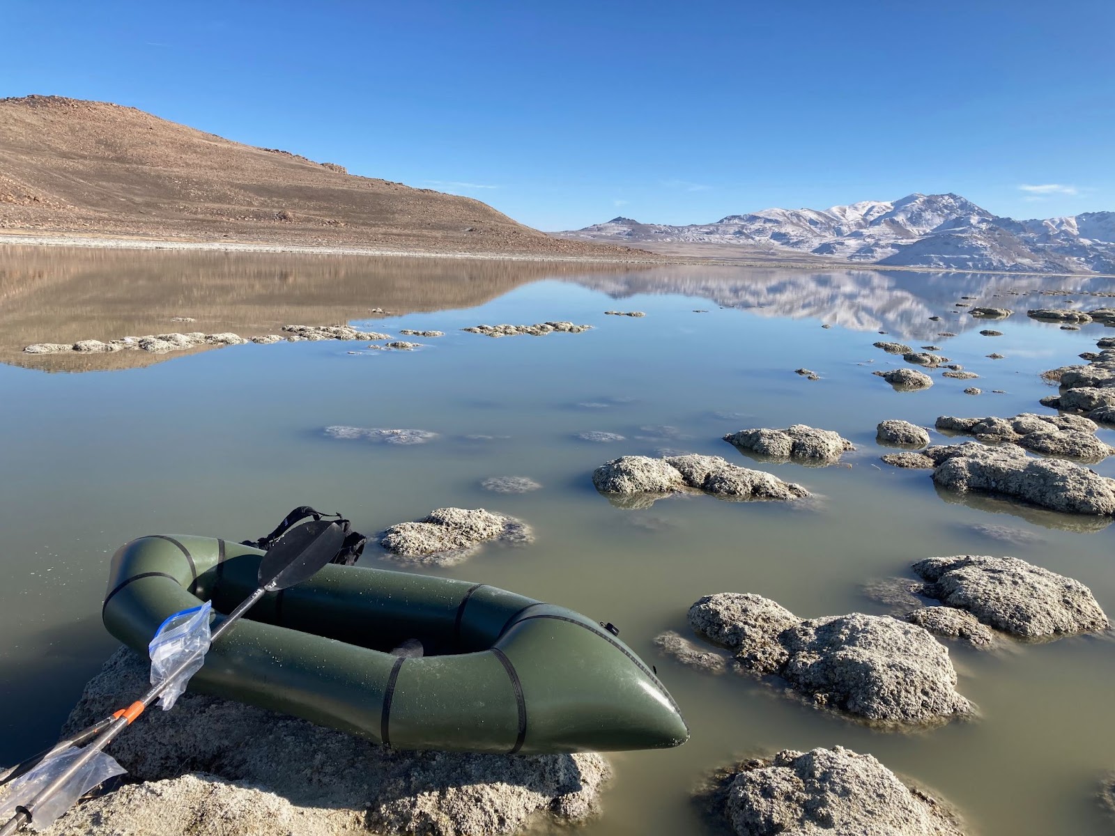 An Alpacka Scout sits on a rock in the middle of a receding lake