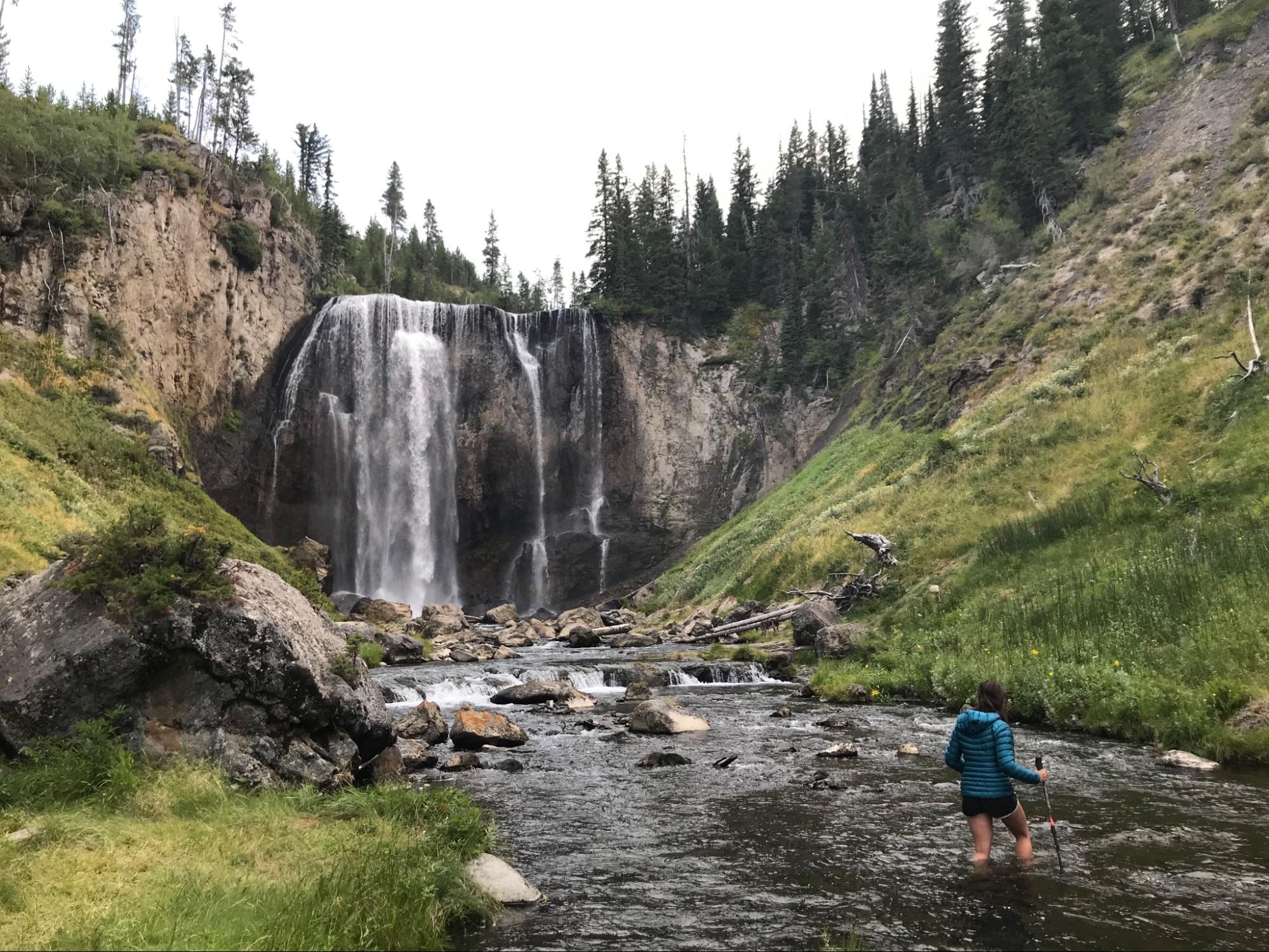 a person standing in a river next to a waterfall