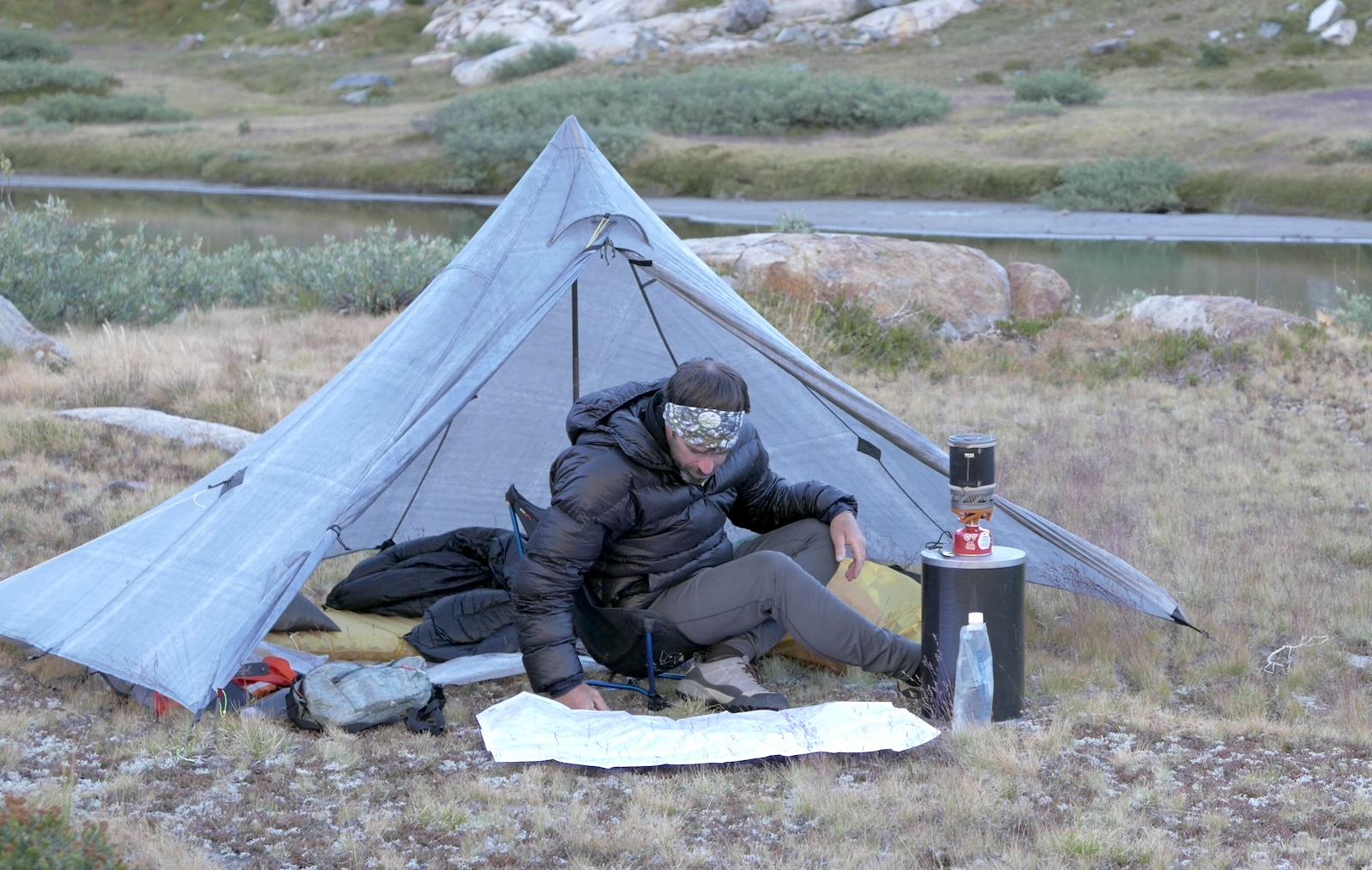 a man sitting in front of a tent on top of a field