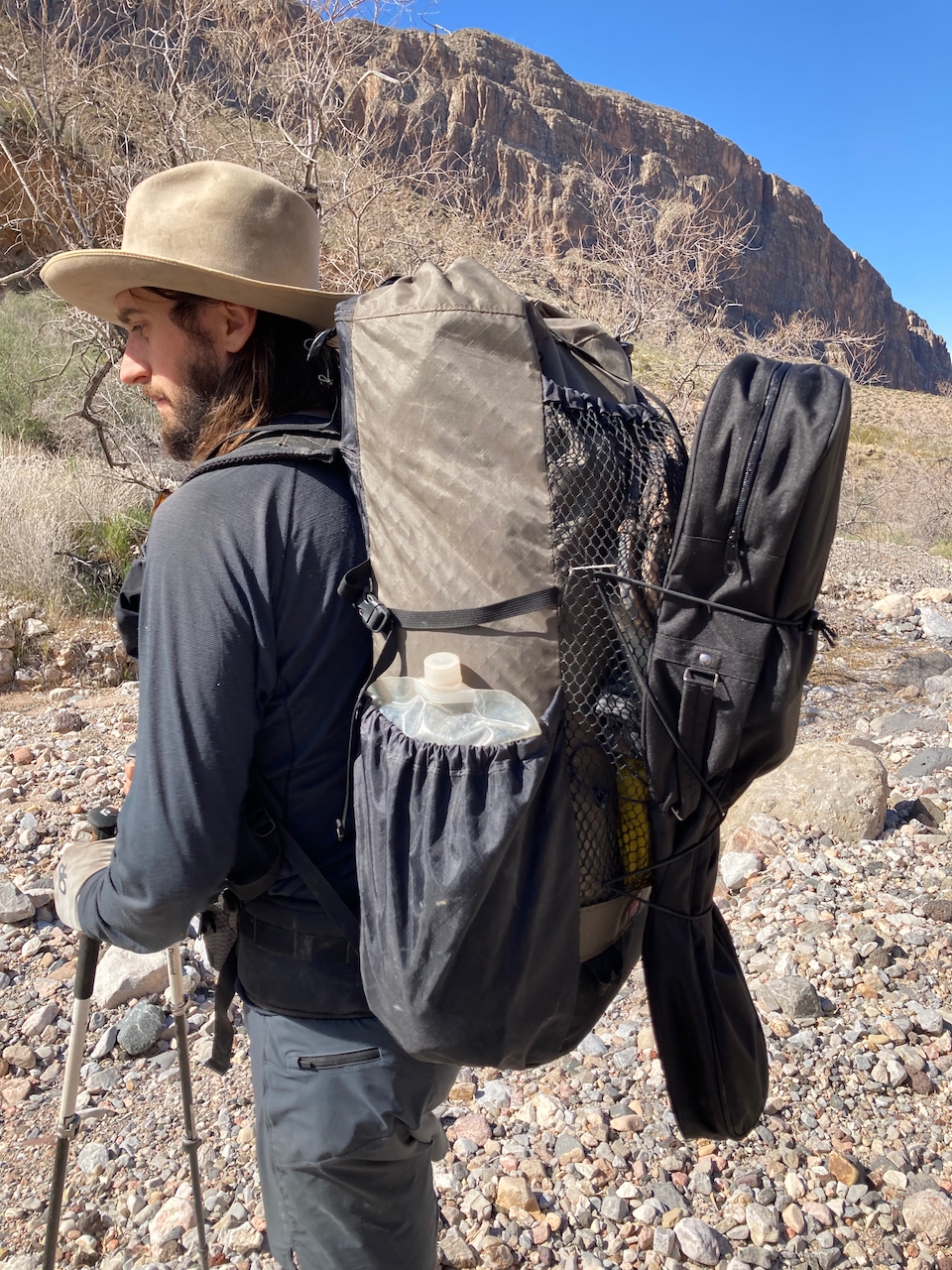 A man carries a backpack loaded down with a guitar and lots of water. 