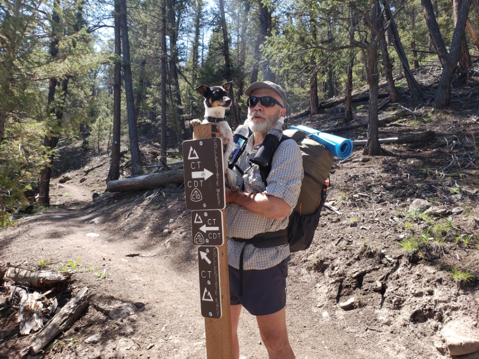 a man with a backpack and a dog standing next to a sign