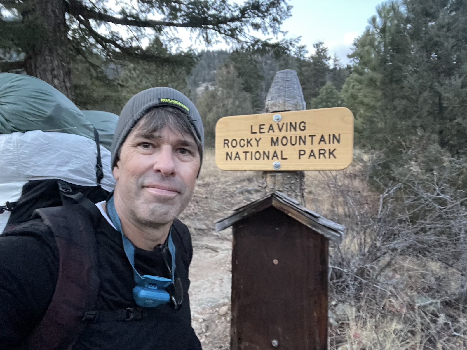 a man standing in front of a sign that says leaving rocky mountain national park