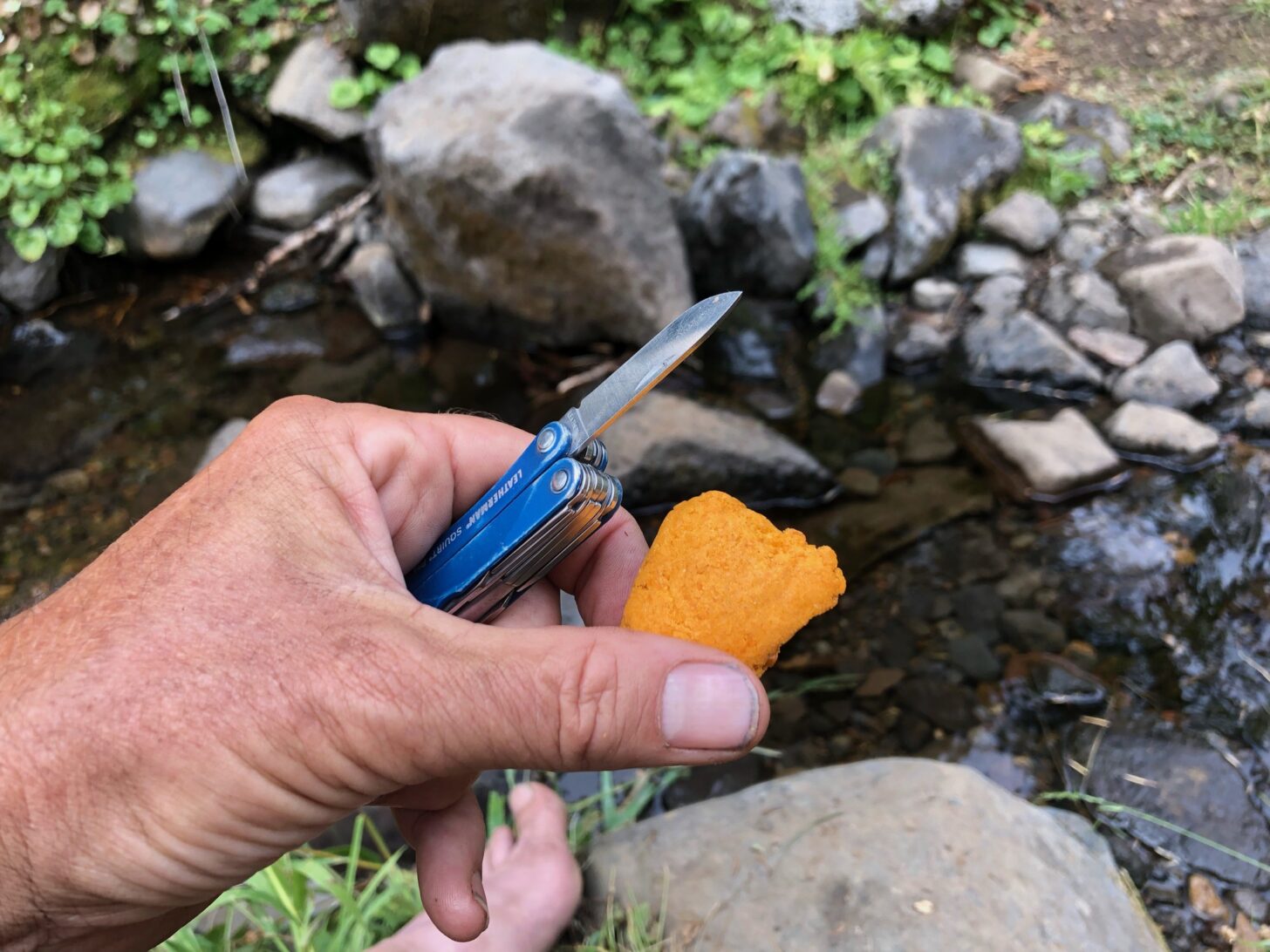 A hand holding a knife and a chunk of freeze-dried mango smooth