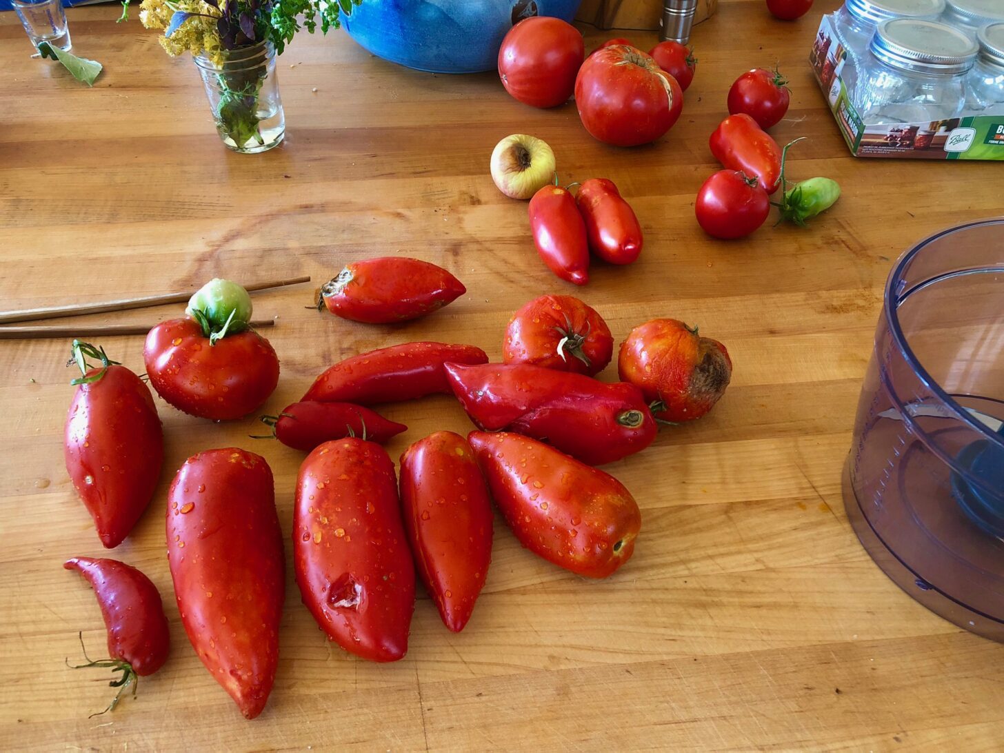 a collection of delicious looking, home-grown tomatoes sitting on a butcher block, surrounded by food processing tools.