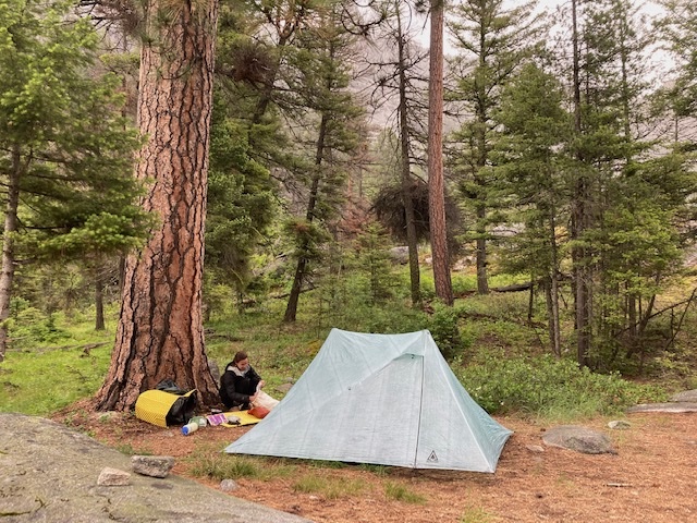 person sitting by a tent in the forest