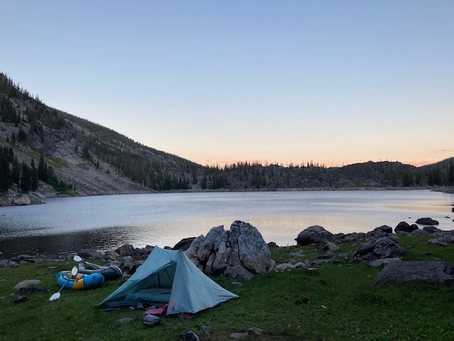 tent pitched by a mountain lake with packrafts on shore