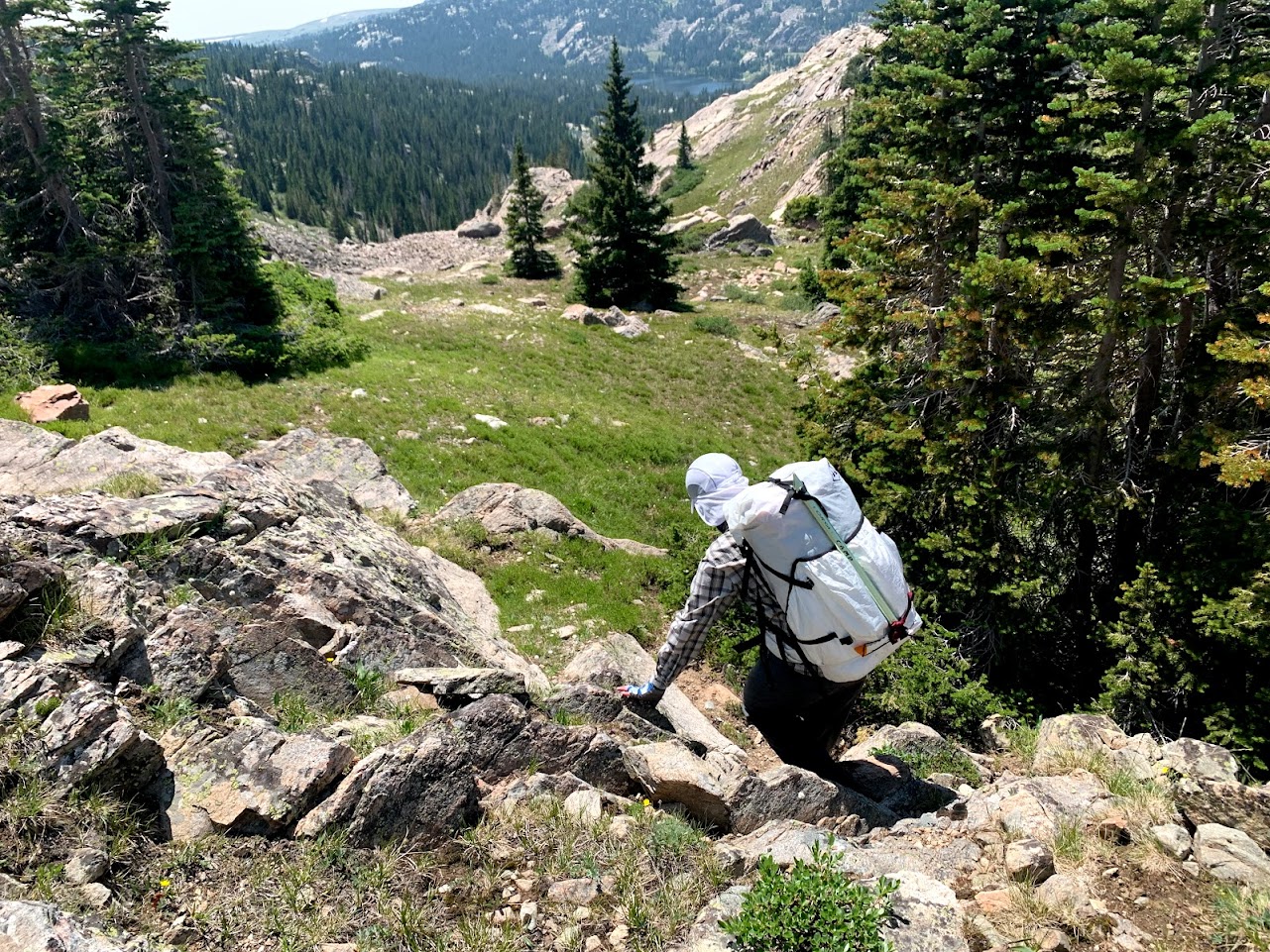 a man wearing a small pack scrambles down a jumble of rocks.