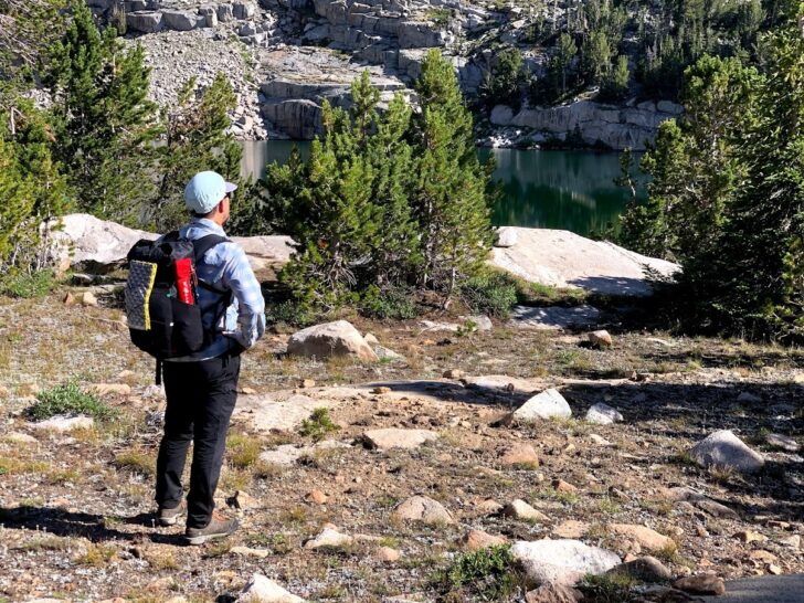 a man stands facing away from the camera while wearing a small backpack.