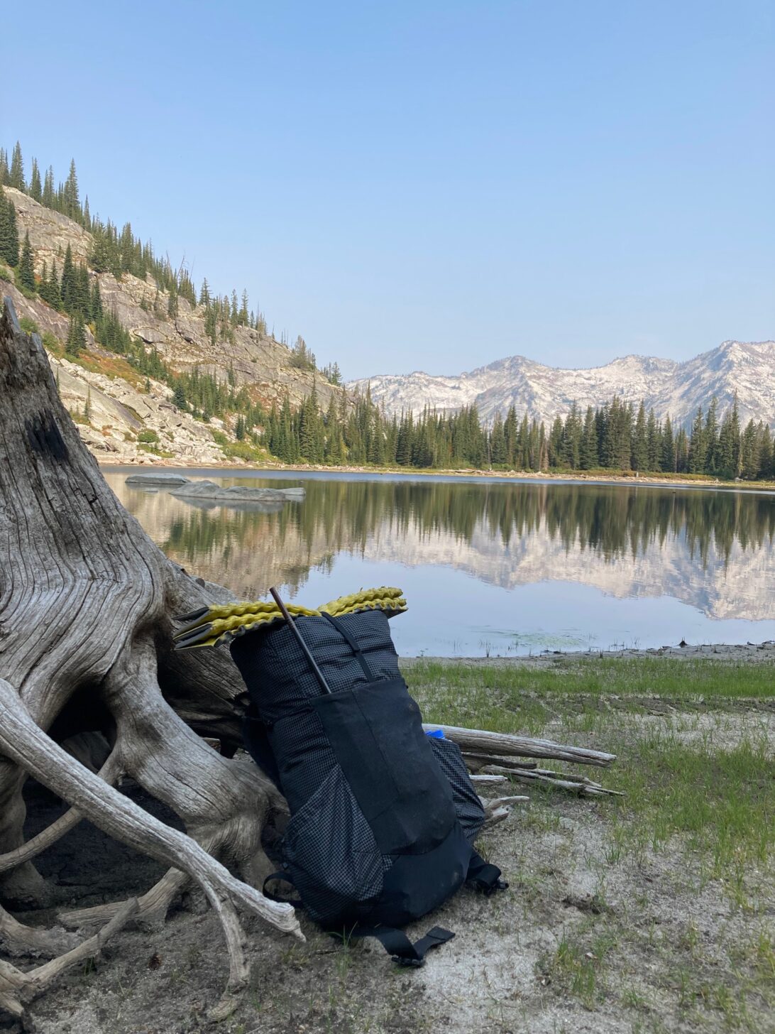 a black backpack on the banks of an alpine lake. A sit pad is strapped to the top and a fishing pole is sticking out of it.