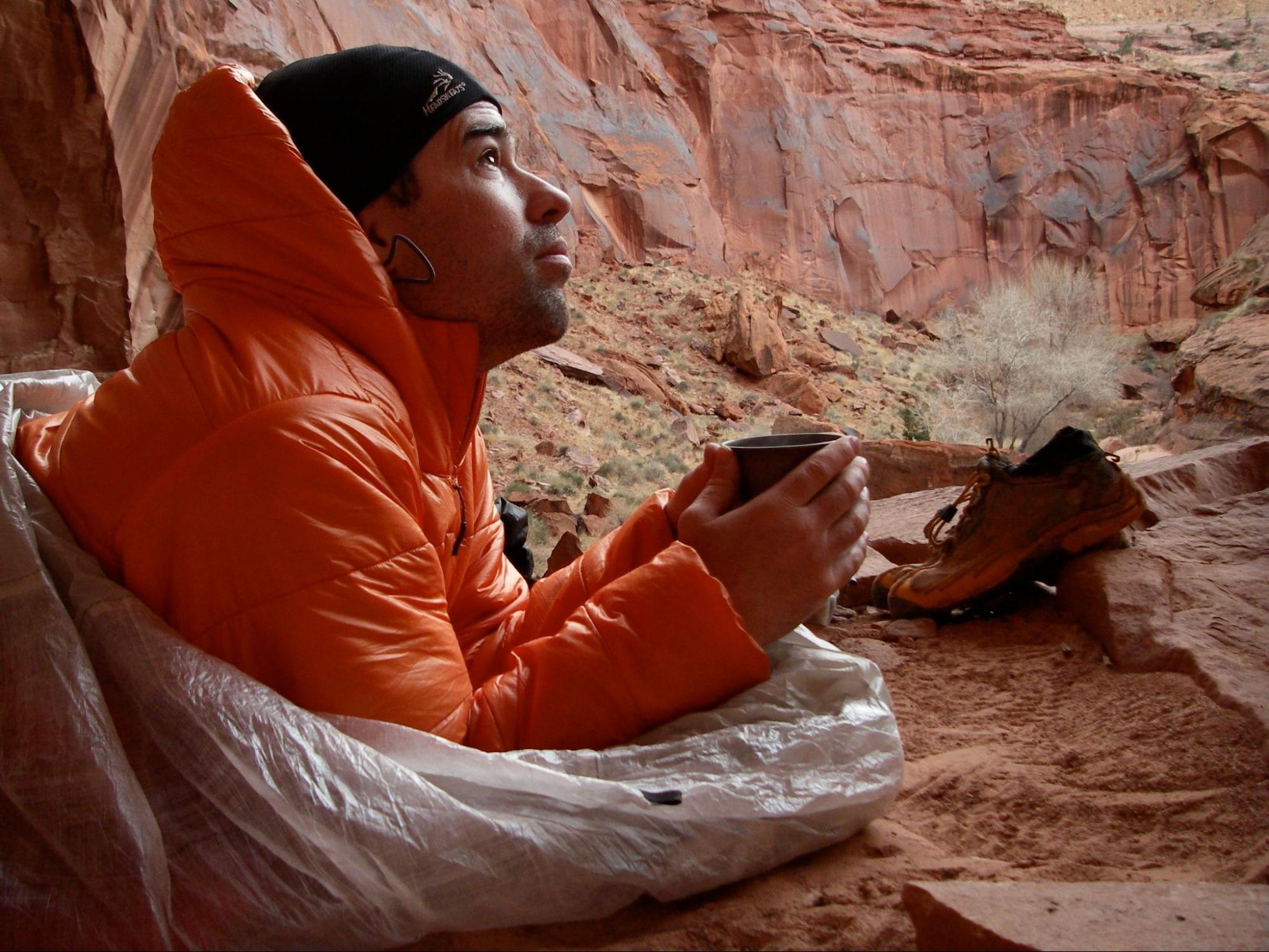 a man in an orange jacket sitting on a rock