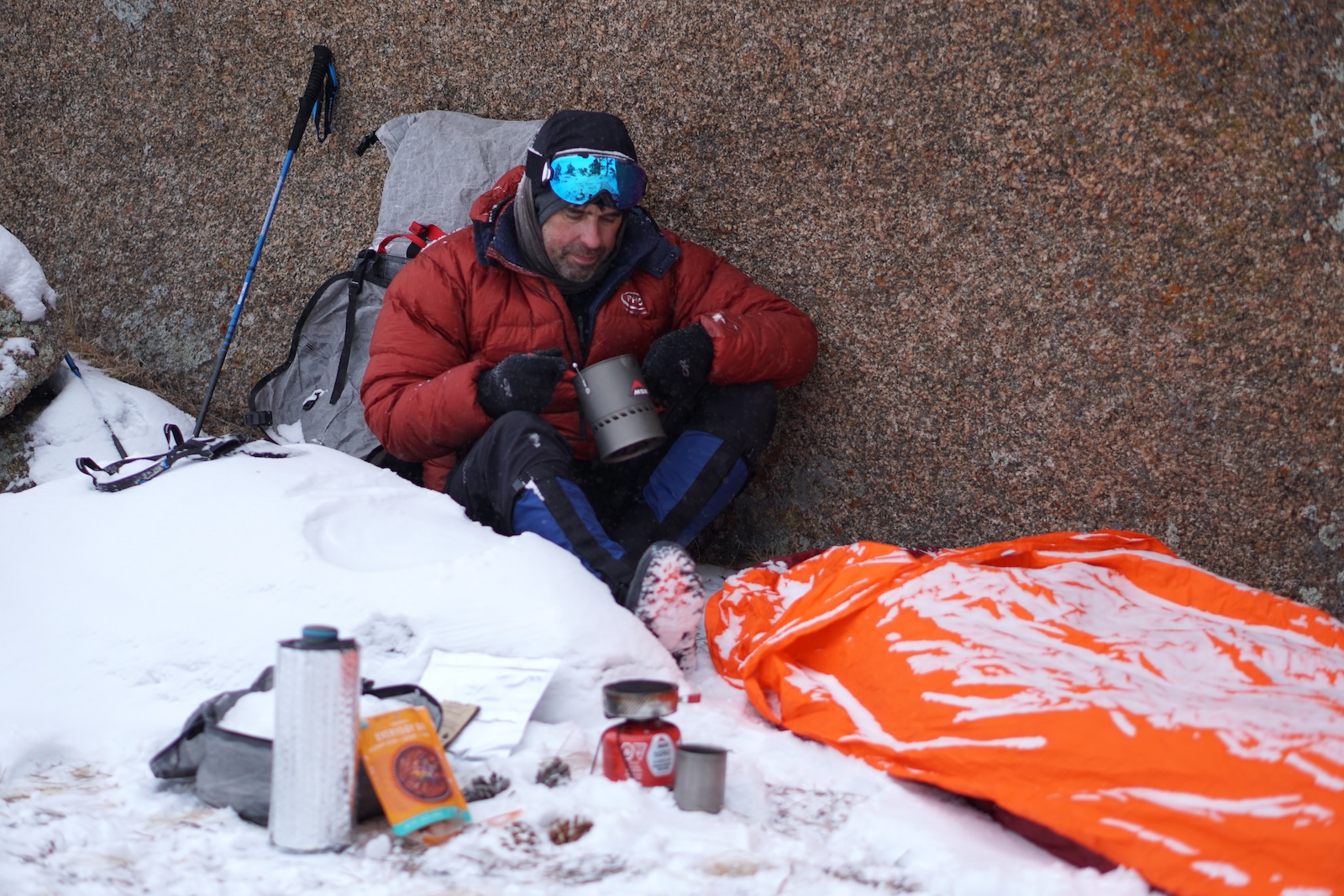 a man sitting in the snow next to a sleeping bag