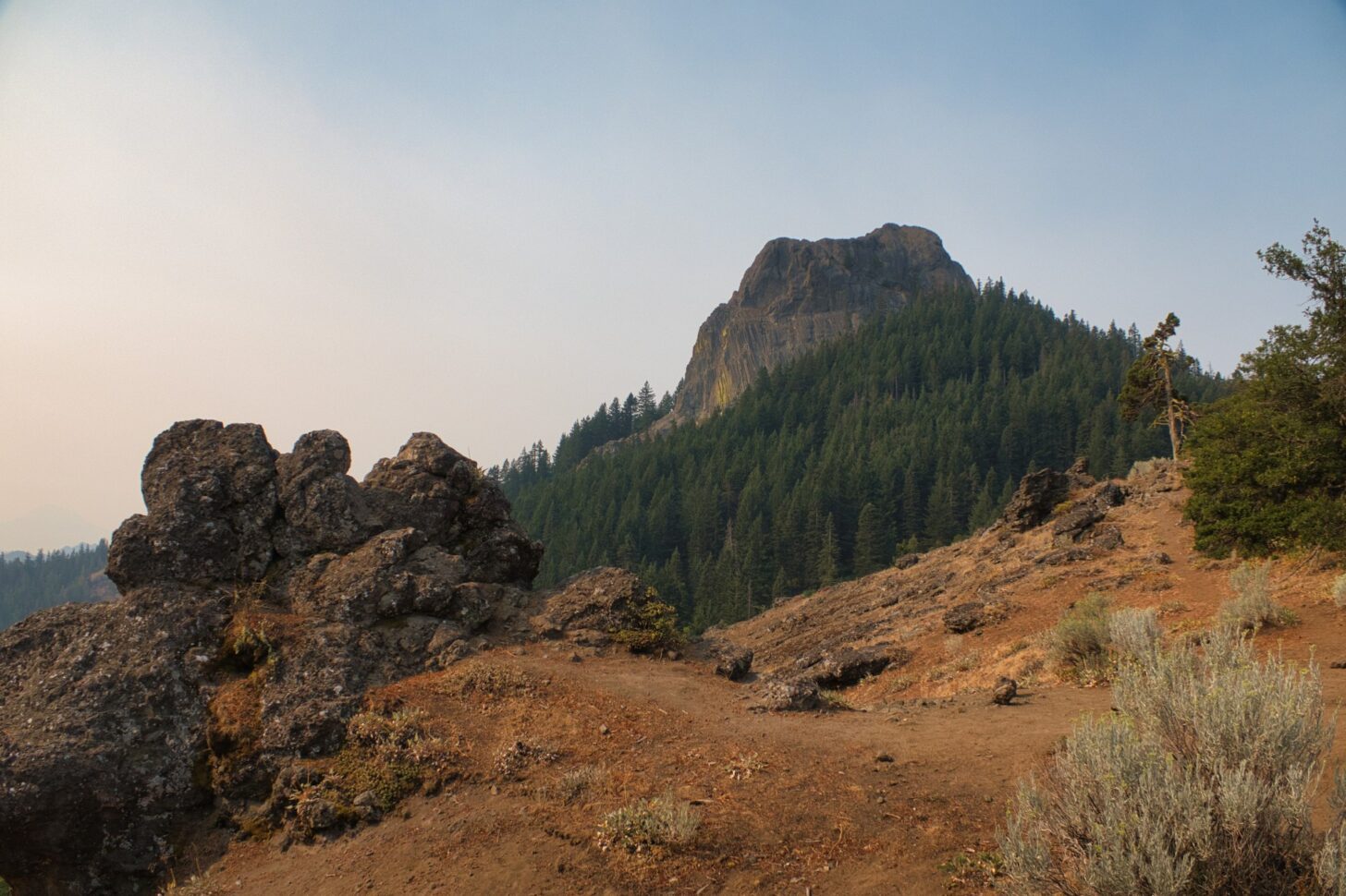 A mountain looms high above in the background. In the foreground, bare dirt.