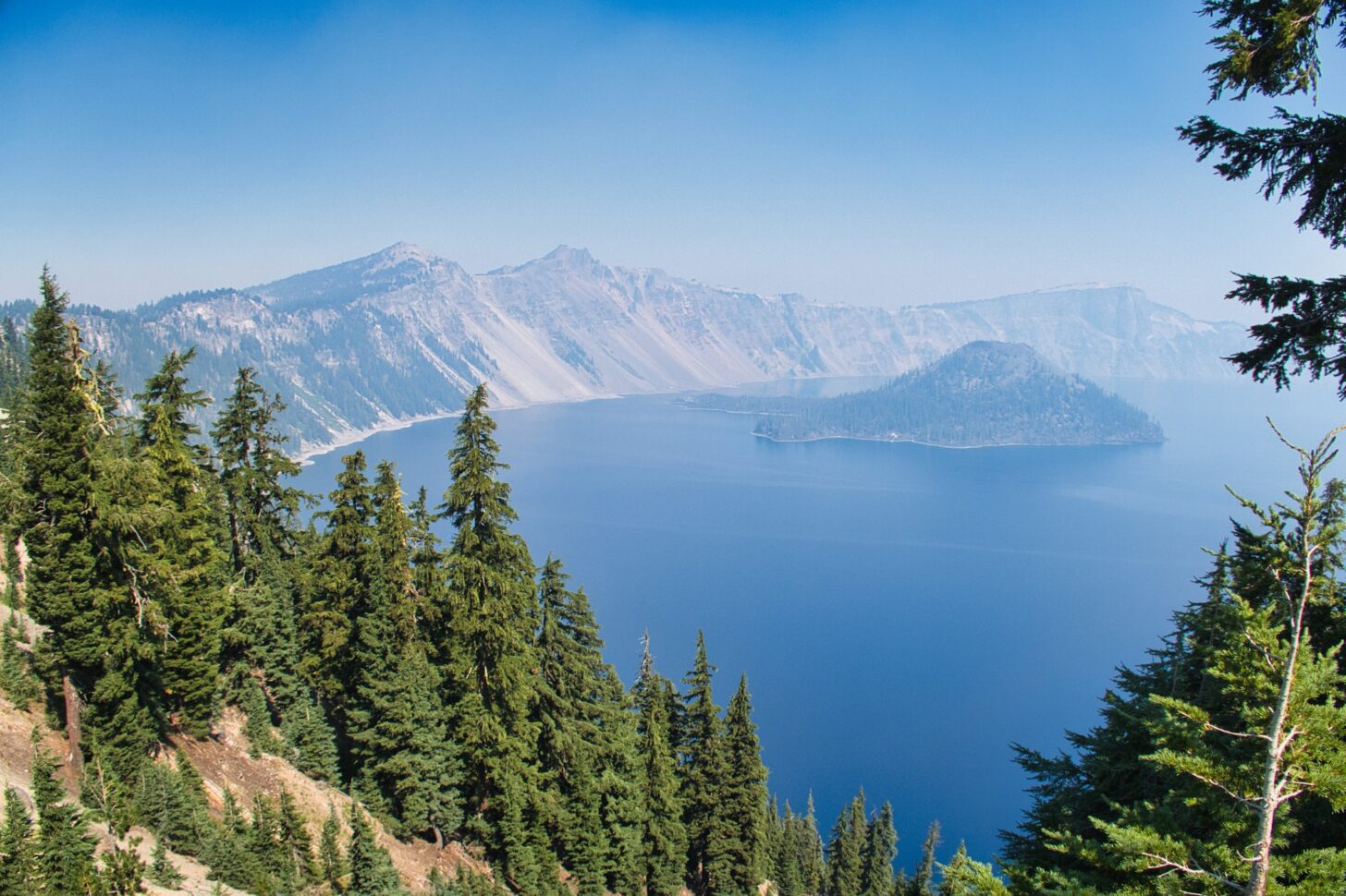 A lake nestled in a huge crater with trees in the foreground.