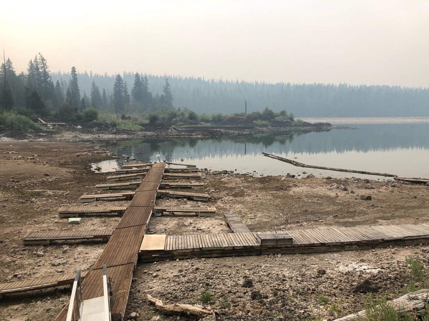 a lake has withdrawn past the boat docks. Smoke is in the air.