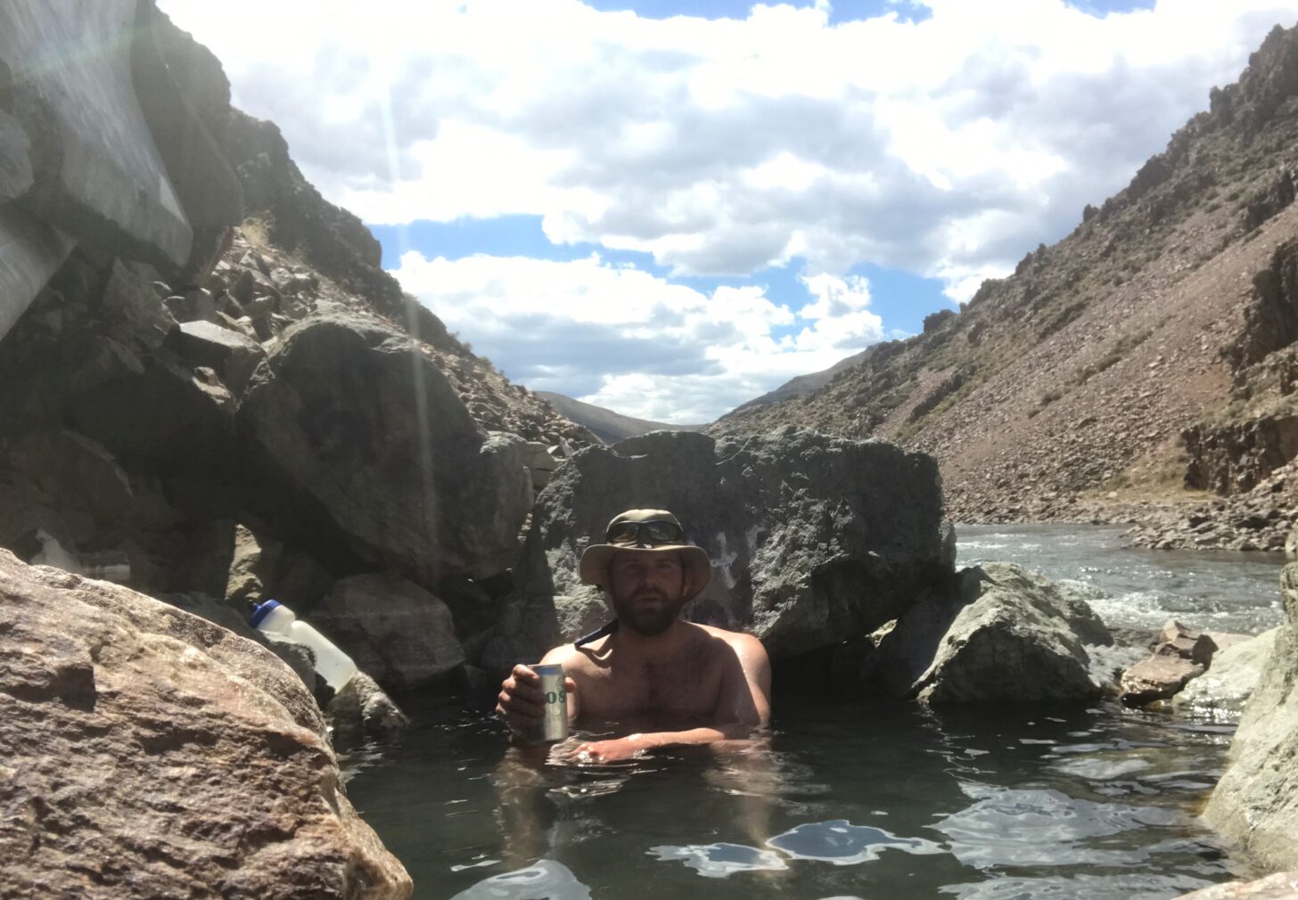 A man sits in a hot spring next to a river.